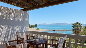 Una terraza de madera con una mesa y sillas, con vista a una playa y un mar azul cristalino.