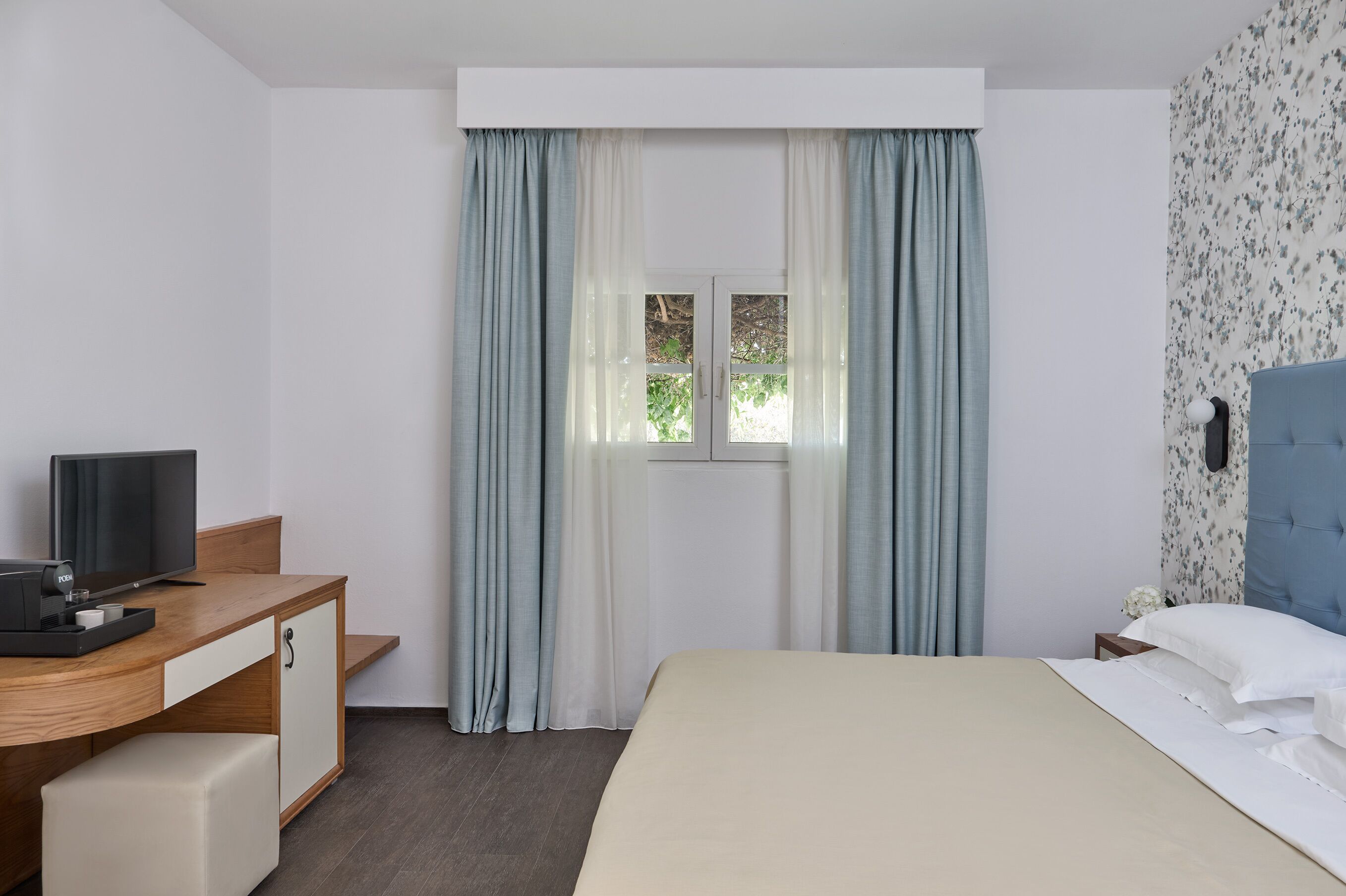 Ett hotellrum med en säng, ett skrivbord med en tv och ett fönster med gardiner.