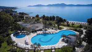 Un resort con una amplia piscina, sillas de descanso y sombrillas, rodeado de vegetación y vistas al mar.