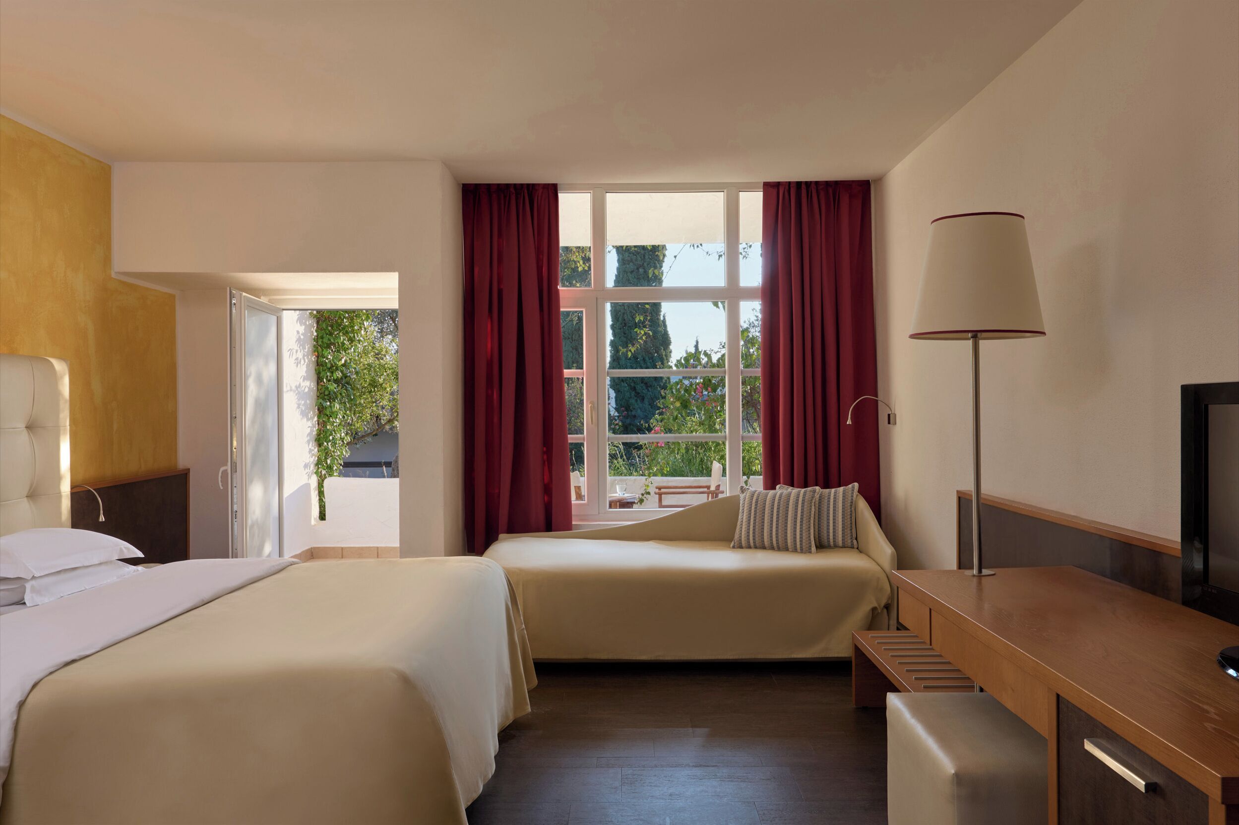 A hotel room with two beds, a desk, a TV, and a window with curtains.