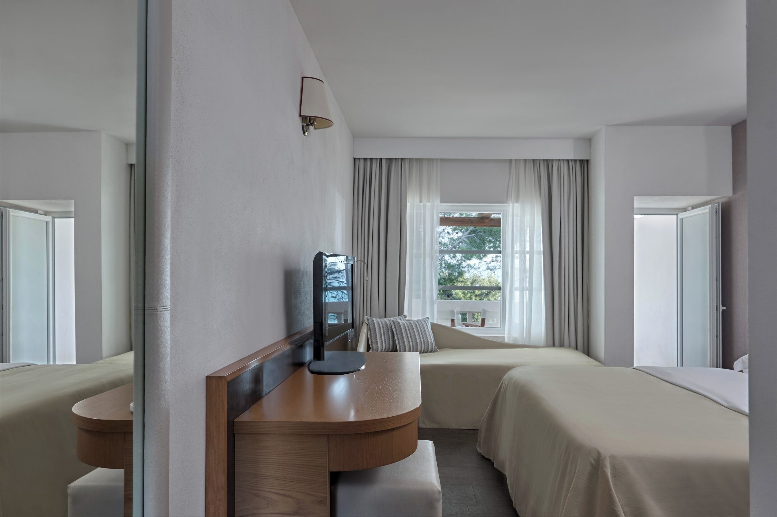 A hotel room with a bed, a desk, a chair, a lamp, and a window with curtains.