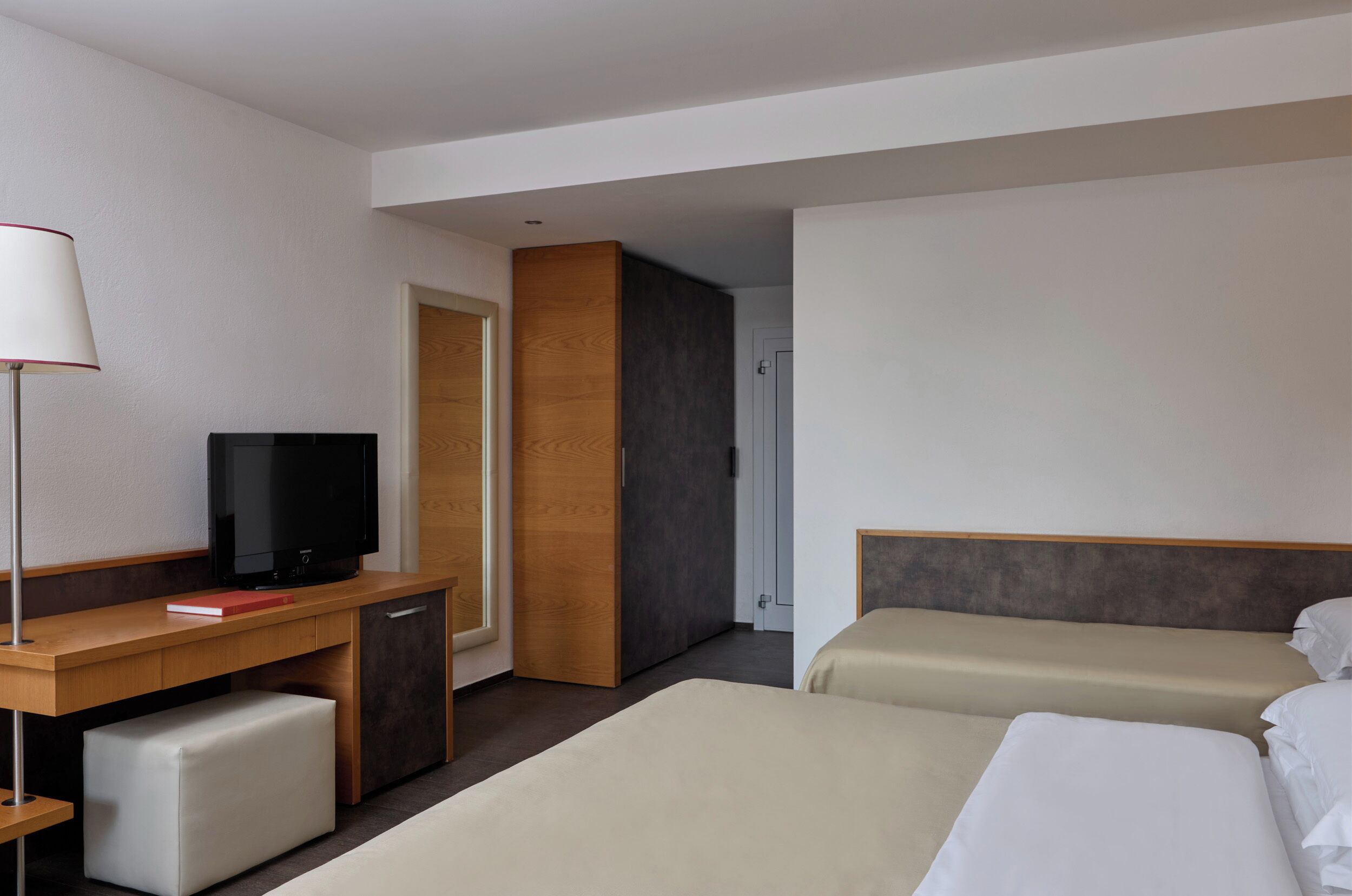 A hotel room with a desk, TV, two beds, and a wardrobe.