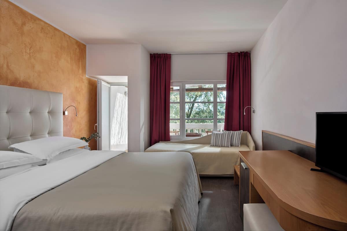 A hotel room with two beds, a desk, a TV, and a window with curtains.