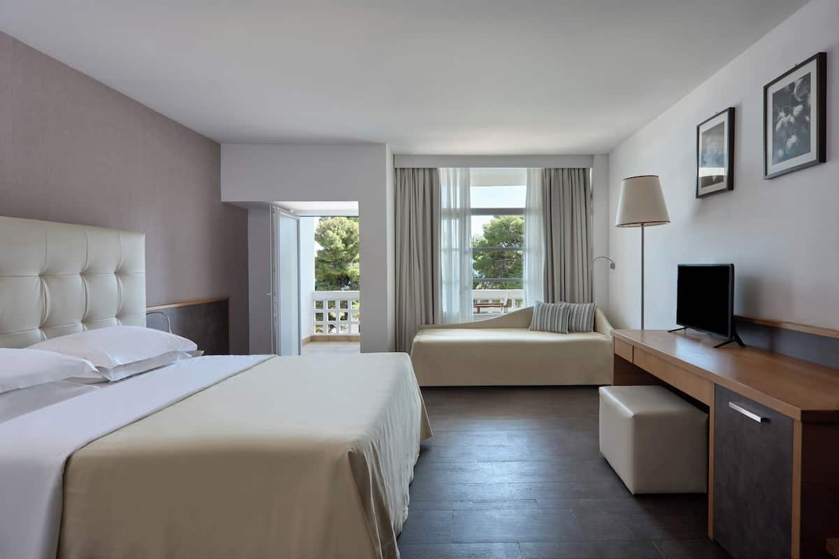 A hotel room with a bed, a sofa, a desk, a TV, and a balcony with a view.