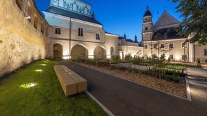 A courtyard with a pathway, benches, and a building with arched windows and a tower. - Domus Maria (Vilnius)