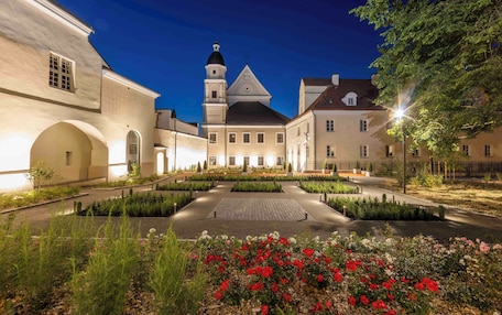 A historic building with a central courtyard, a tower, and a well-maintained garden with red flowers.
