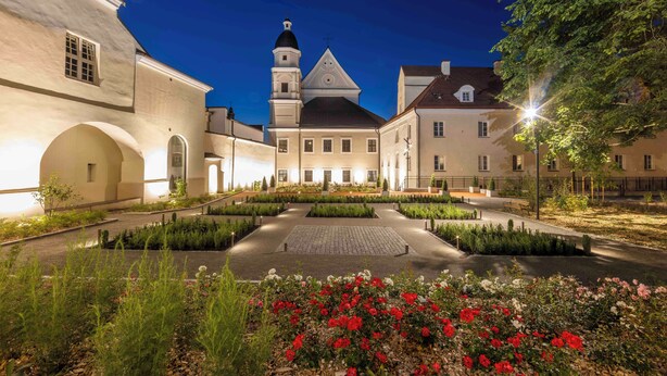 A historic building with a central courtyard, a tower, and a well-maintained garden with red flowers. - Domus Maria (Vilnius)
