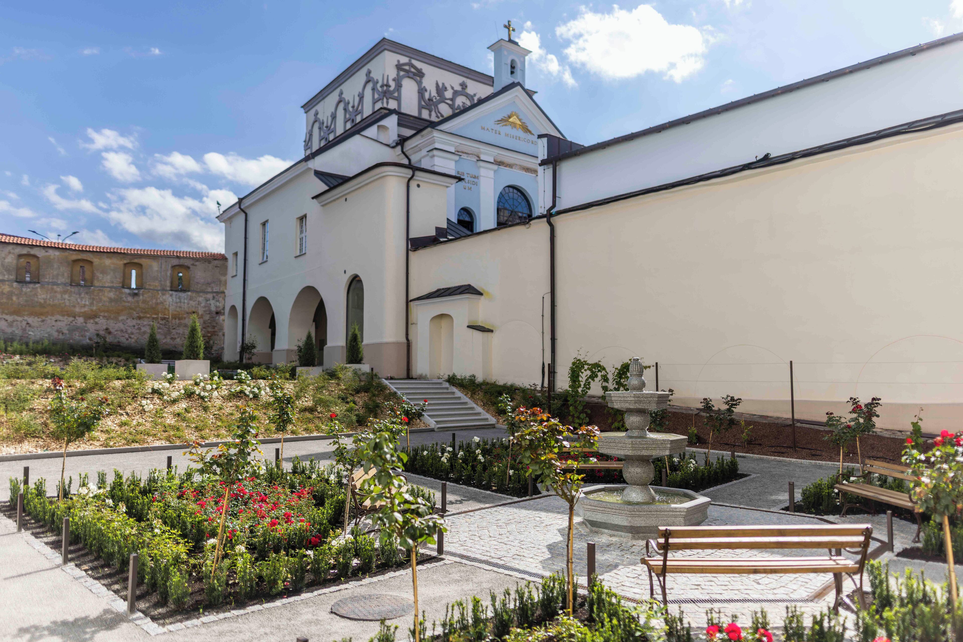 Un patio con una fuente, bancos y un edificio con un campanario.