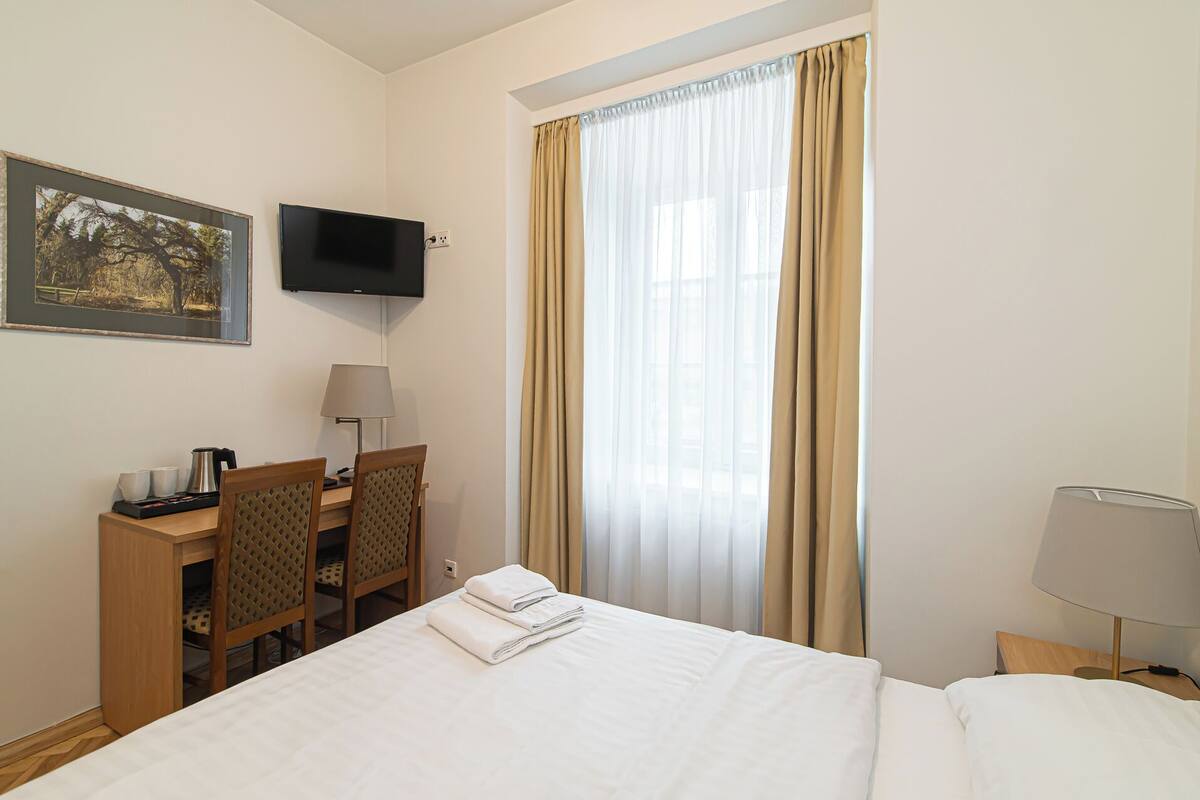 Une chambre d’hôtel comprenant un lit, un bureau avec une chaise, une télévision et une fenêtre avec des rideaux.