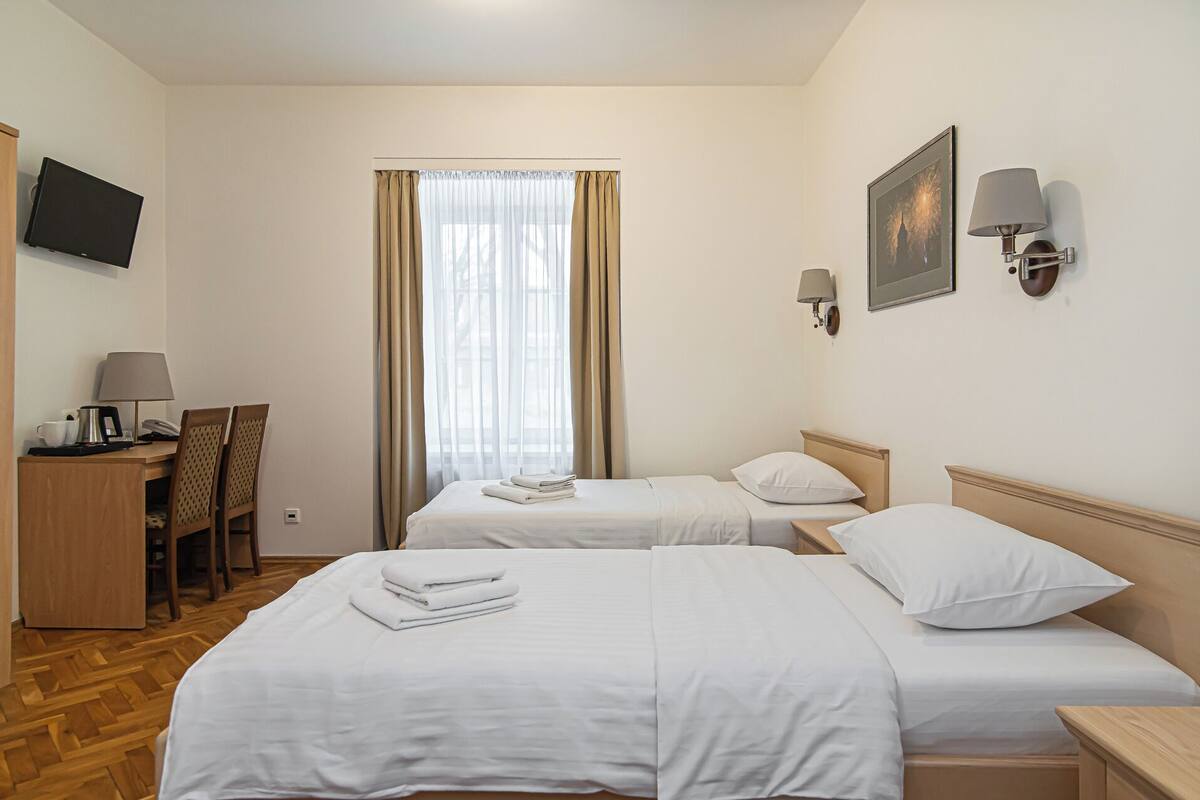 Une chambre d’hôtel avec deux lits, un bureau doté d’un téléphone et d’une machine à café, une chaise et un téléviseur fixé au mur.