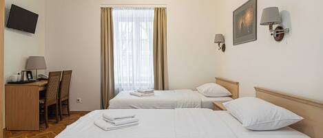 A hotel room with two beds, a desk with a telephone and a coffee maker, a chair, and a television on the wall.