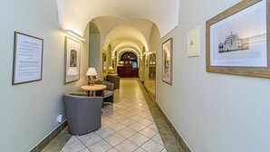 A hotel corridor with arched ceilings, framed pictures on the walls, a reception desk, and a seating area with a lamp. - Domus Maria (Vilnius)
