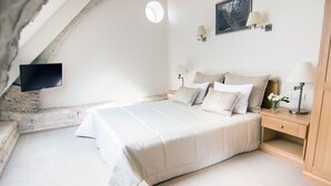 A bedroom with a bed, bedside tables, a flat-screen TV mounted on the wall, and a stone wall. - Domus Maria (Vilnius)