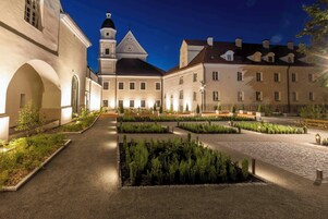 Un cortile con un giardino centrale, circondato da edifici dall'architettura classica, tra cui una chiesa con campanile.