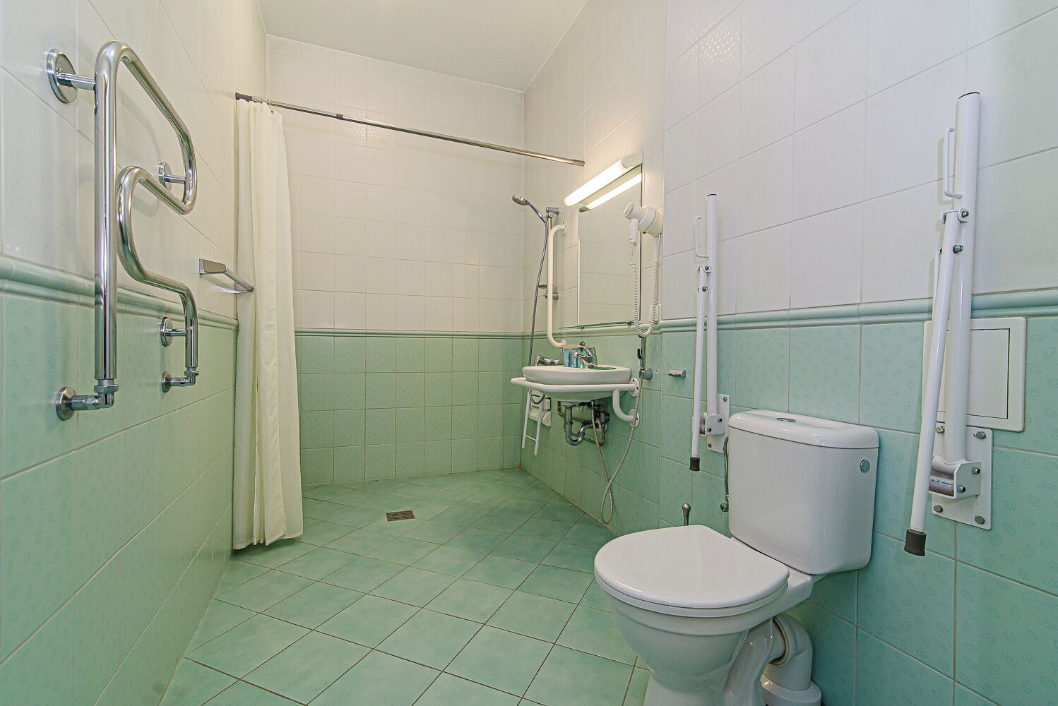 Een badkamer met toilet, wastafel en douchegedeelte, voorzien van handgrepen en een rolstoeltoegankelijke douche.