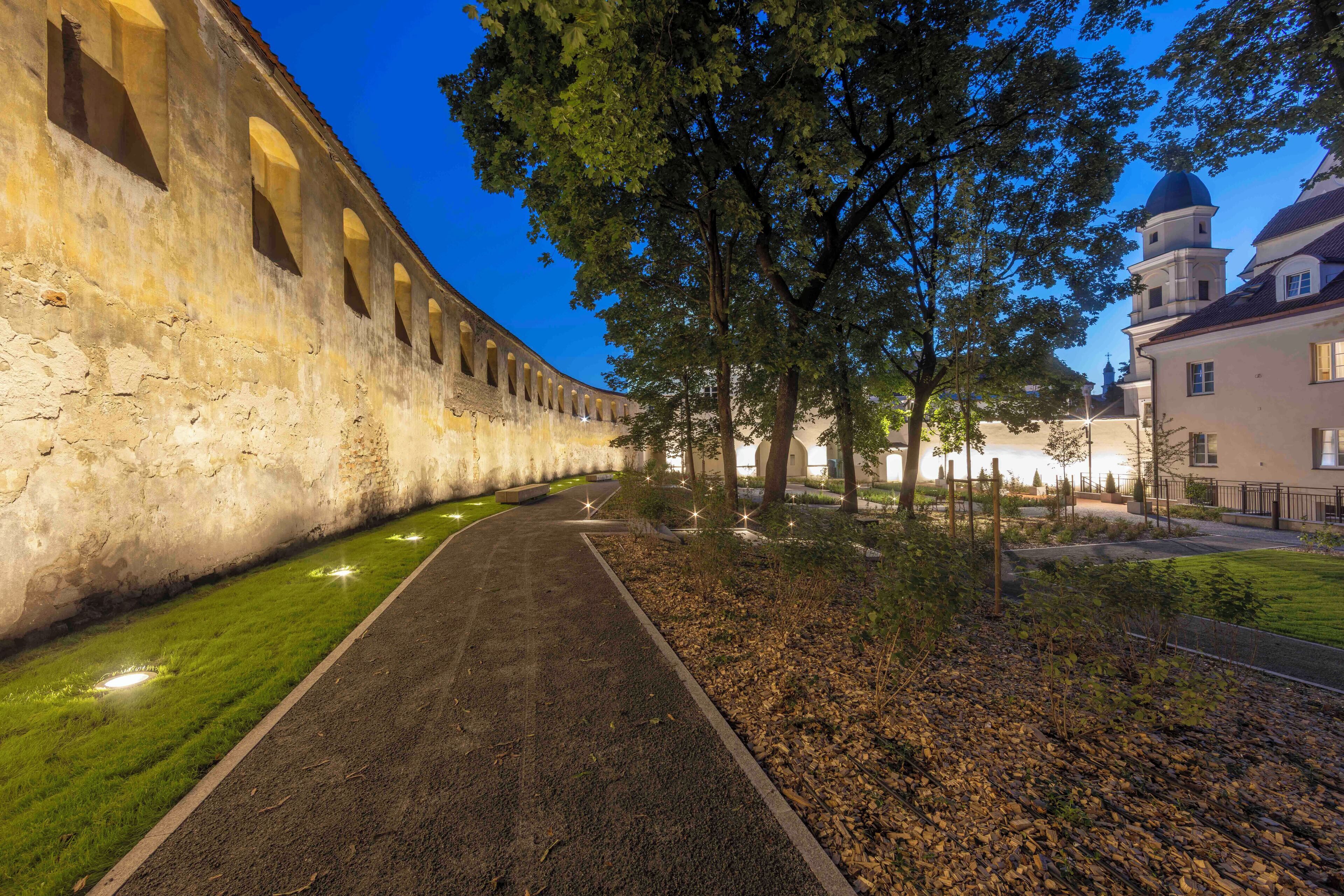 A pathway flanked by a historic building with arched windows and a dome structure.