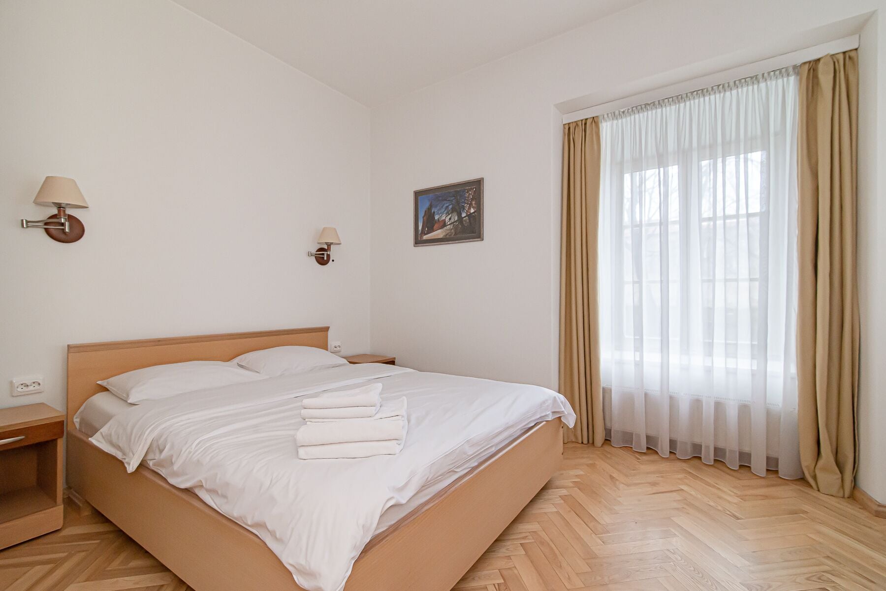 A neatly made bed with white linens, a wooden headboard, and a nightstand with a lamp.