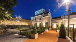 A courtyard with a brick pathway, potted plants, and a building with arched windows and a mural. - Domus Maria (Vilnius)