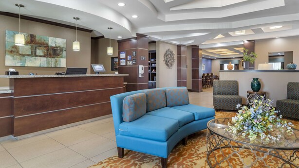 A reception area with a blue sofa, a glass coffee table, and a reception desk. - Best Western Plus Longhorn Inn & Suites (Luling)