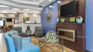 A modern lobby with a blue sofa, patterned chairs, a fireplace, and a flat-screen TV mounted on the wall. - Best Western Plus Longhorn Inn & Suites (Luling)