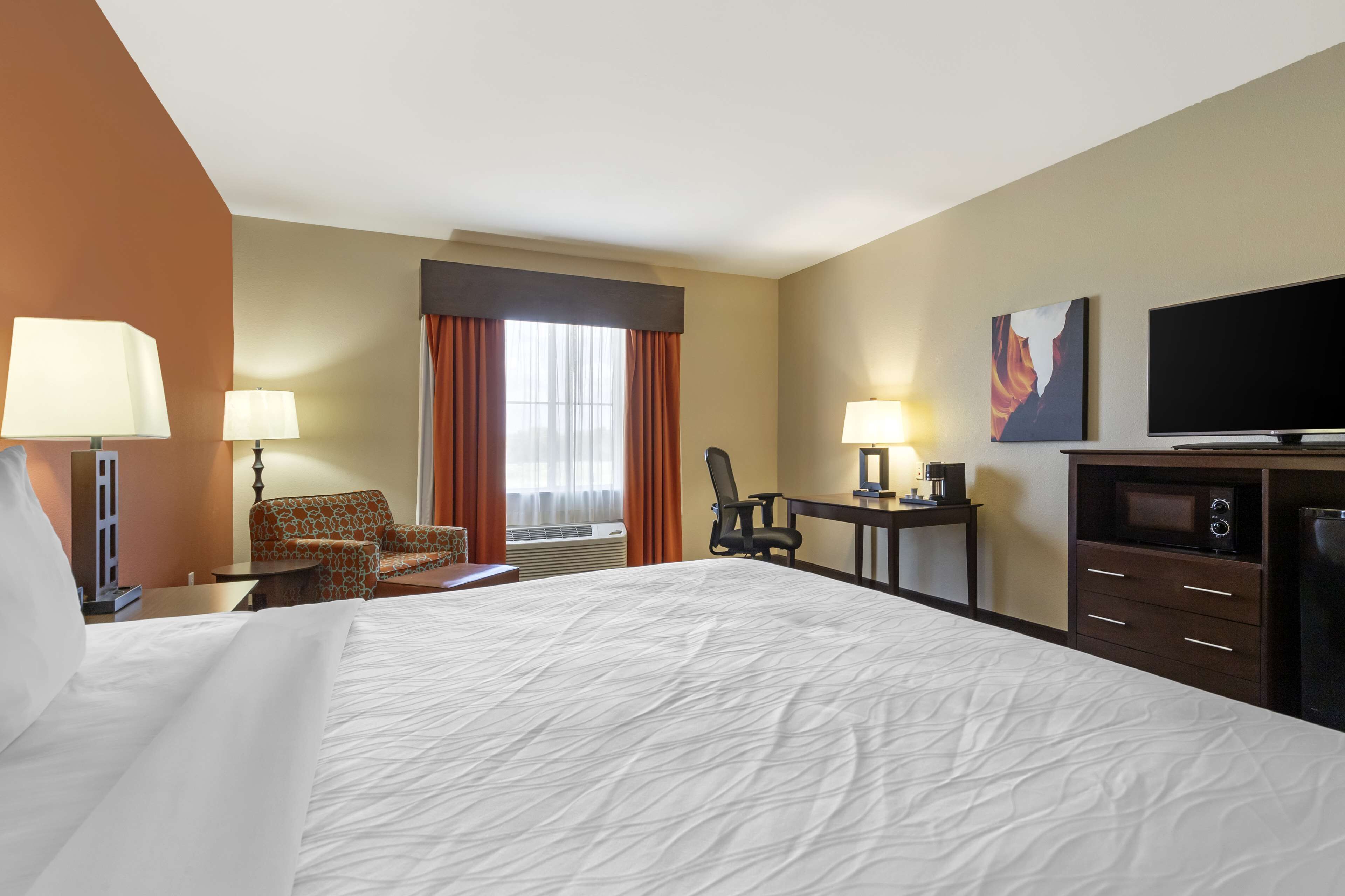 Une chambre d’hôtel avec un grand lit, deux fauteuils, un bureau, une télévision et un four à micro-ondes.