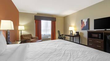 Une chambre d’hôtel avec un grand lit, deux fauteuils, un bureau, une télévision et un four à micro-ondes.