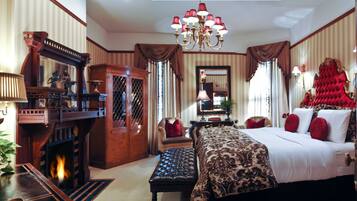 A traditional room with a large bed, a wooden wardrobe, a fireplace, and a chandelier.
