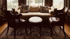 Una habitación de esquina con un gran ventanal, un sofá, dos sillones y una pequeña mesa redonda.