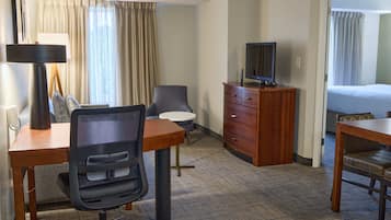 A hotel room with a desk, chair, television, dresser, and a bed.