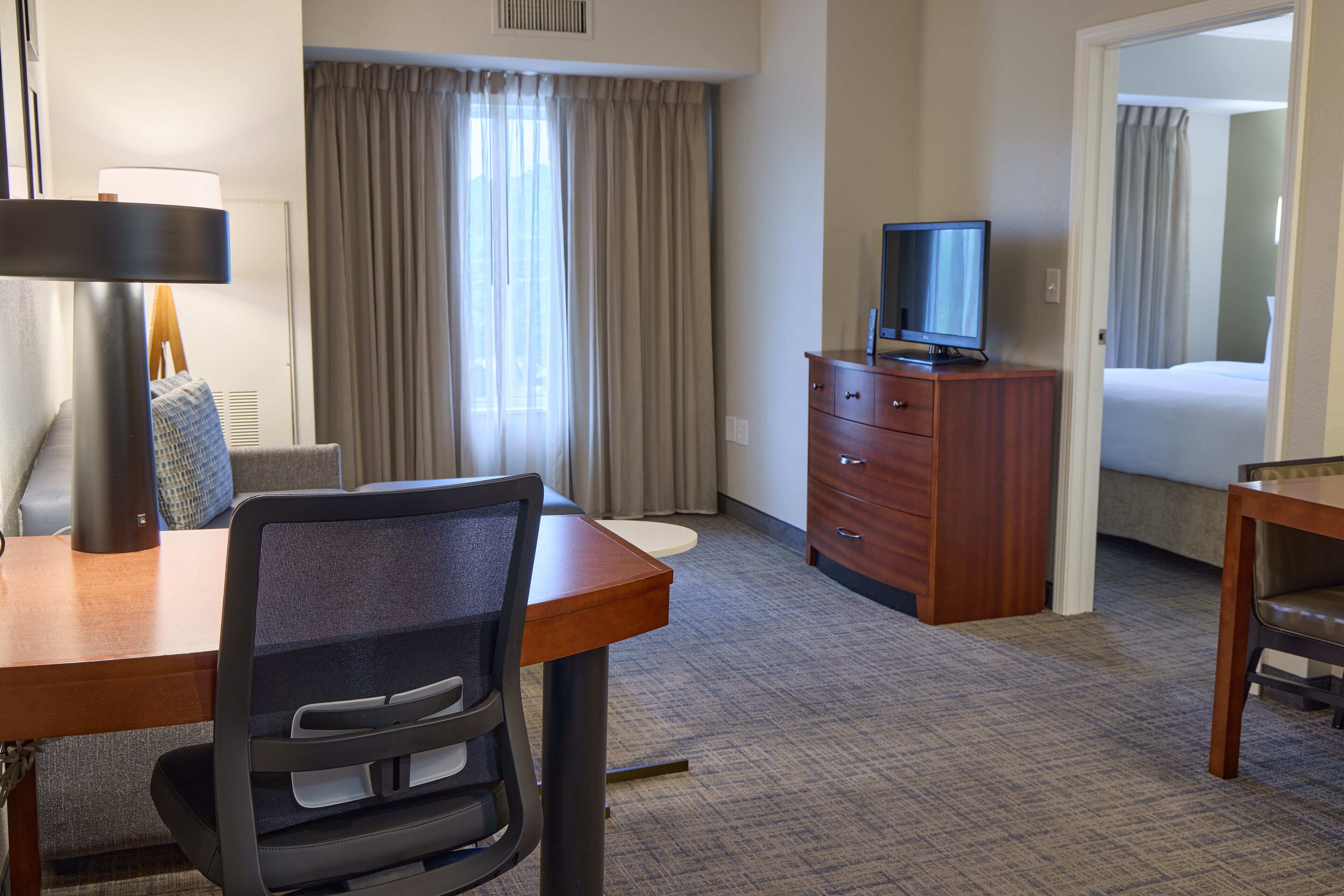Une chambre d’hôtel équipée d’un bureau, d’une chaise, d’une télévision, d’une commode et d’un lit.