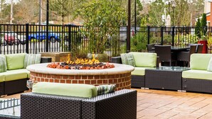 An outdoor seating area with a brick fire pit, green cushioned sofas, and wicker tables. - Residence Inn by Marriott Columbia Northwest/Harbison (Irmo)