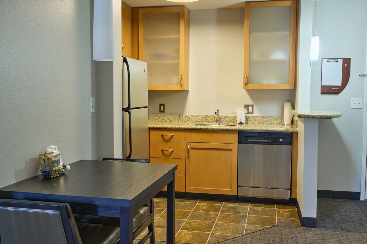 A compact kitchen with wooden cabinets, a stainless steel dishwasher, and a granite countertop.
