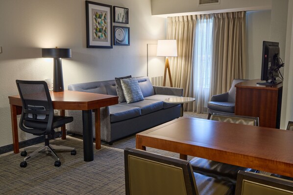 A hotel room with a wooden dining table, a gray sofa, a small round table, a lamp, a TV, and a chair. - Residence Inn by Marriott Columbia Northwest/Harbison (Irmo)