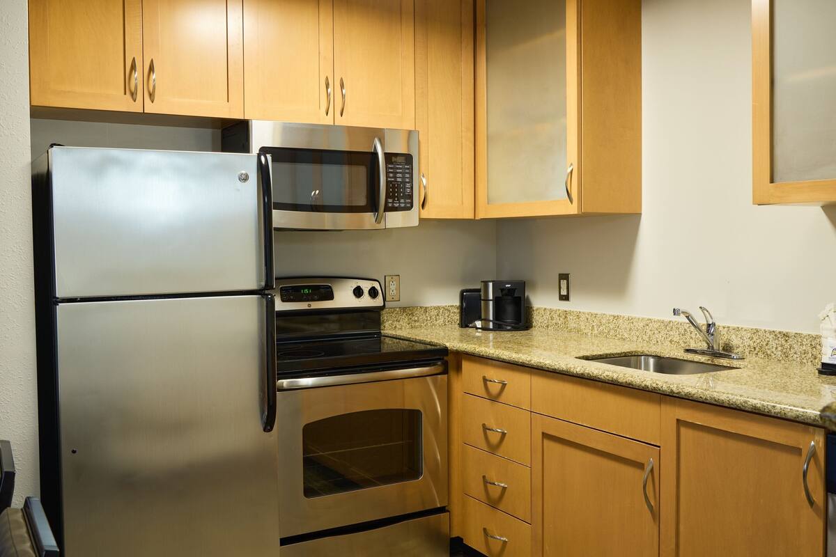 A kitchen with stainless steel appliances, wooden cabinets, and a granite countertop.