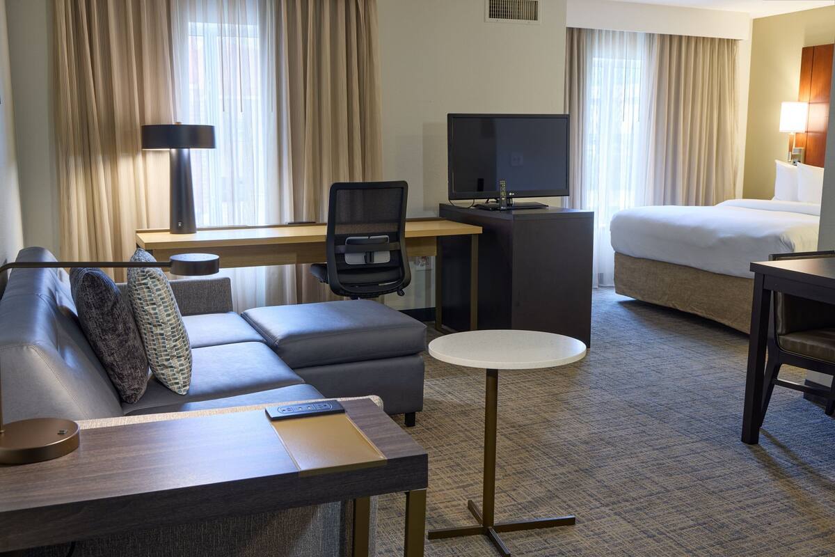 A hotel room with a sofa, a desk with a computer, a bed, and a small round table.