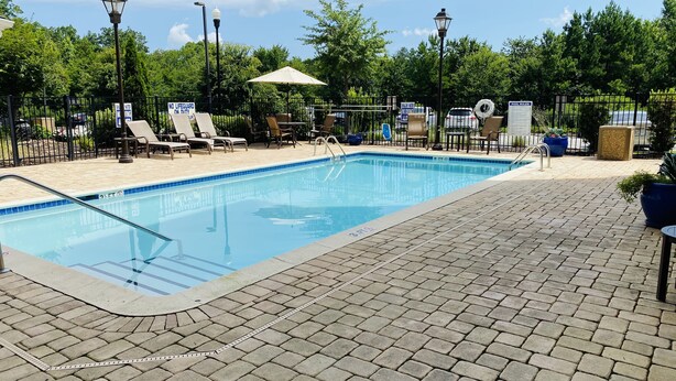 A swimming pool with lounge chairs and umbrellas, surrounded by a fence and trees. - Residence Inn by Marriott Columbia Northwest/Harbison (Irmo)