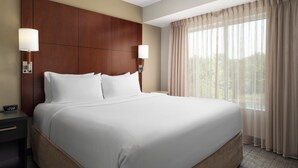 A large bed with a wooden headboard, two bedside lamps, and a window with sheer curtains. - Residence Inn by Marriott Columbia Northwest/Harbison (Irmo)