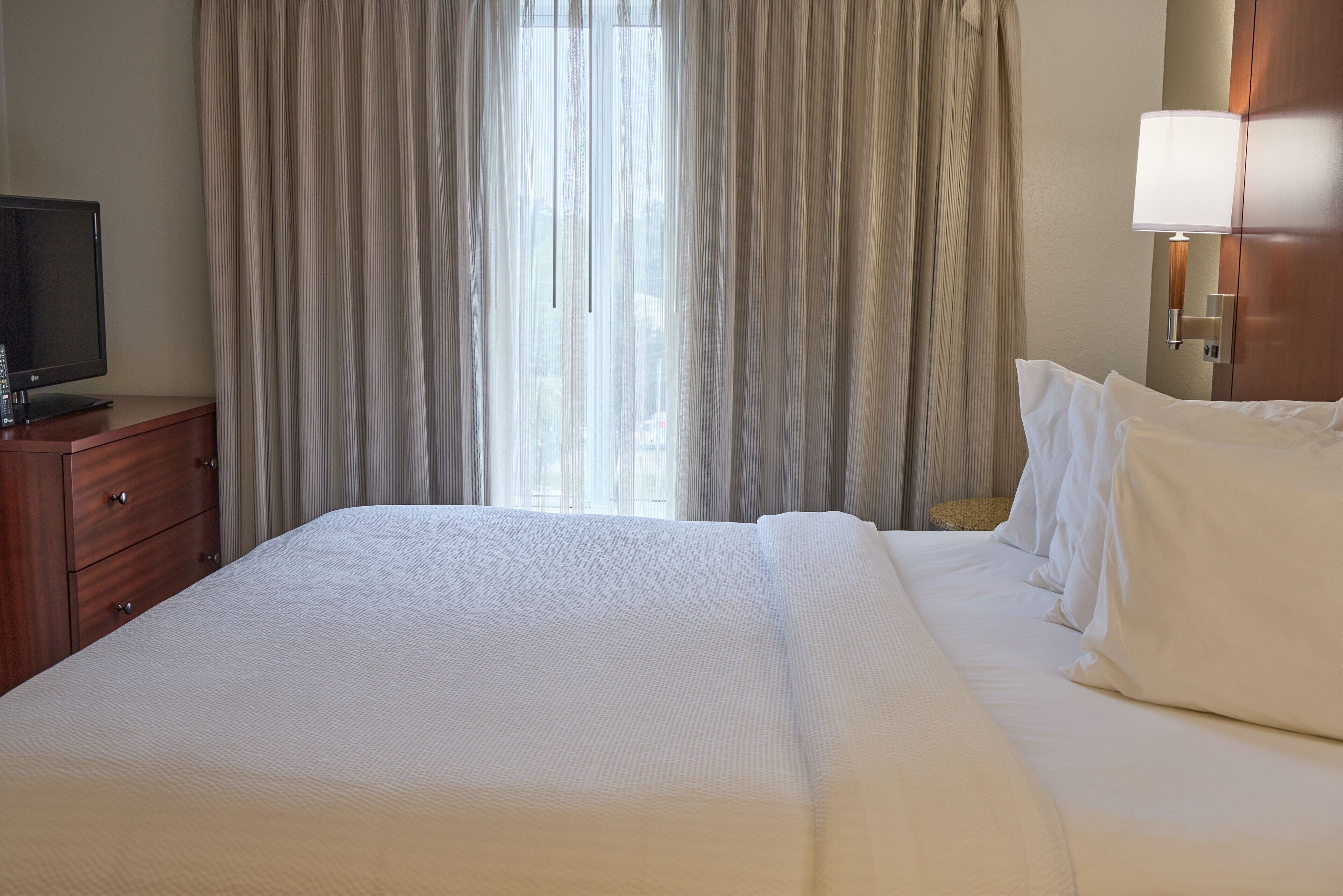 Une chambre d’hôtel avec un grand lit, un téléviseur posé sur une commode en bois et une lampe fixée au mur.