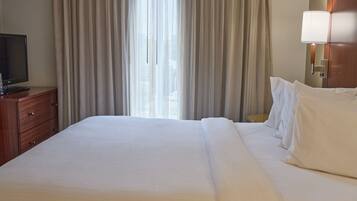 Une chambre d’hôtel avec un grand lit, un téléviseur posé sur une commode en bois et une lampe fixée au mur.