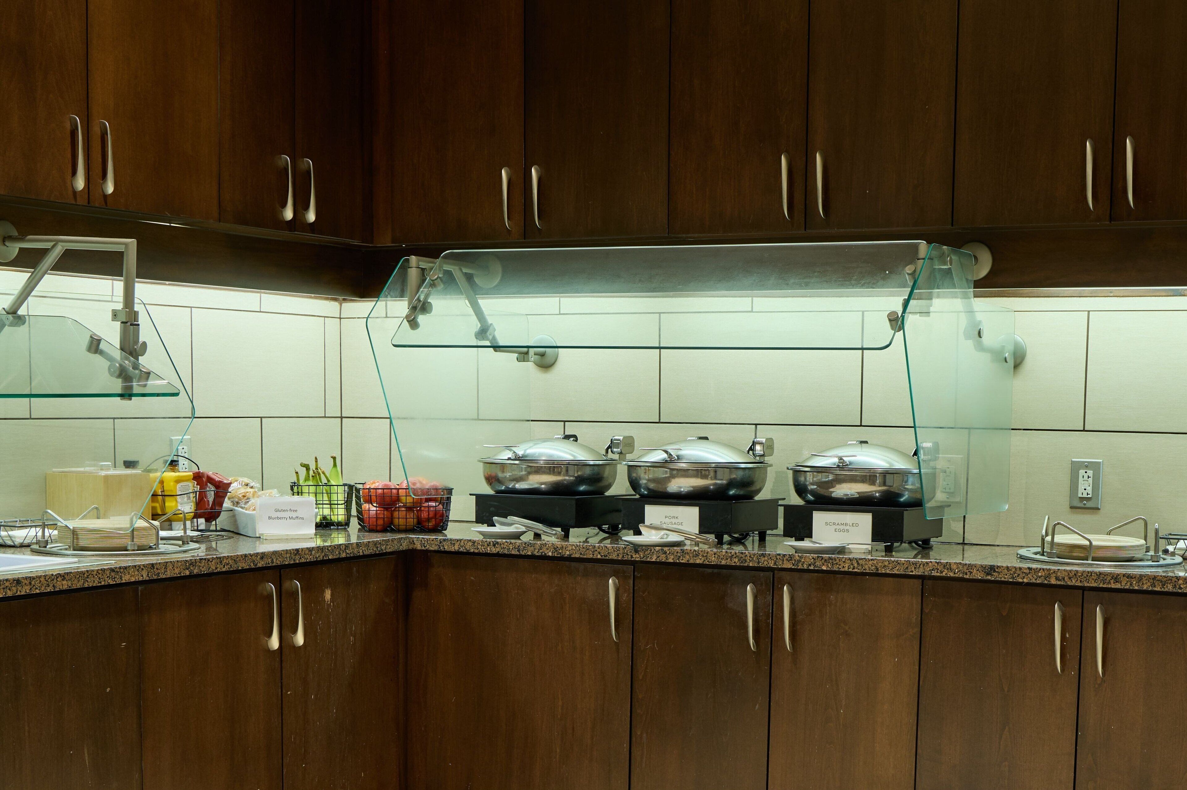 A buffet setup with three covered food stations, a glass display case, and a sink with a faucet.