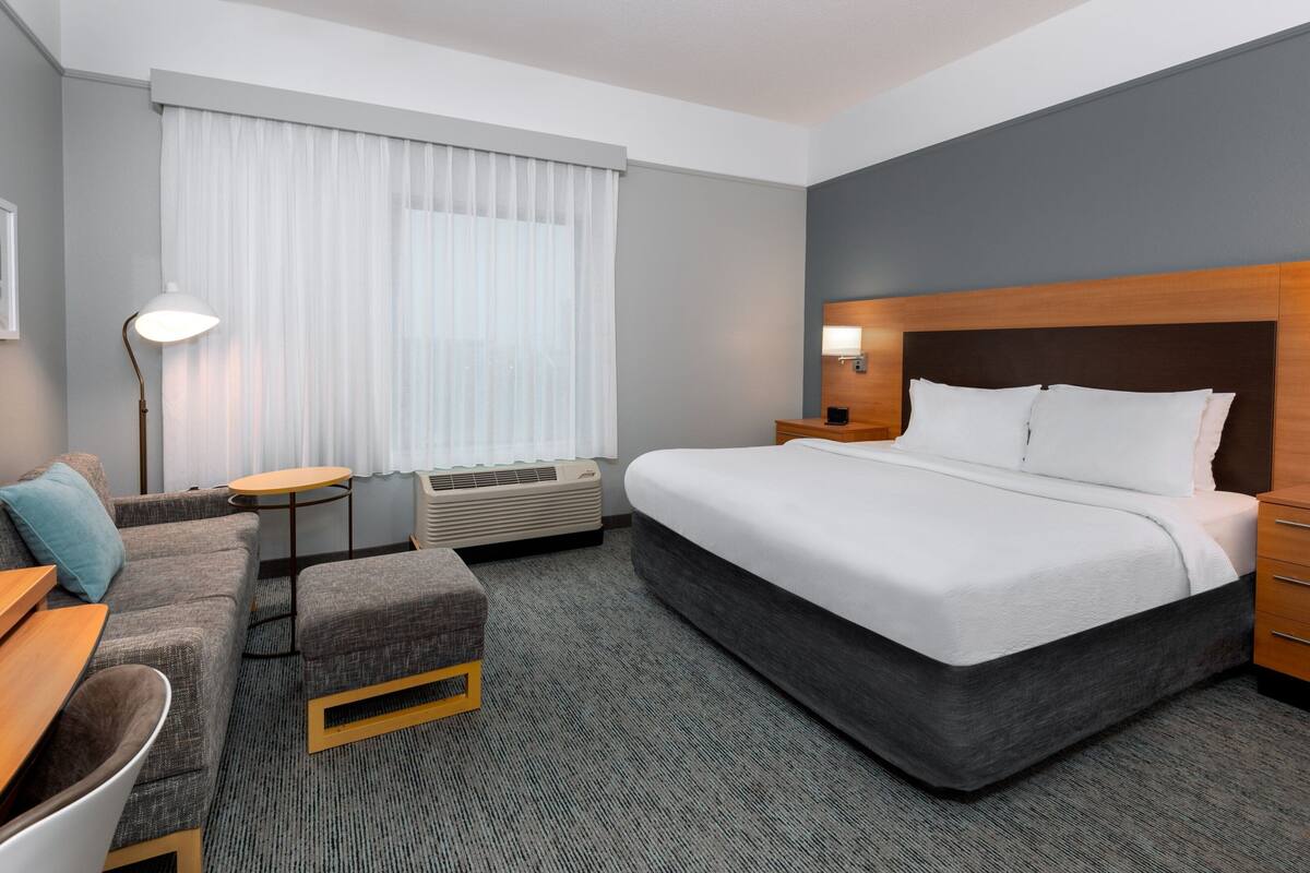 A hotel room with a large bed, a sofa, a small table, and a lamp.