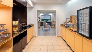 Un moderno vestíbulo de hotel con cocina, zona de estar y un refrigerador lleno de bebidas.