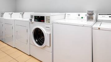 A row of white front-loading washers and dryers in a laundry room.
