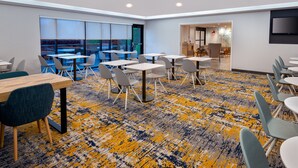 Un moderno salón de conferencias con mesas y sillas, ventanas amplias y suelo alfombrado.