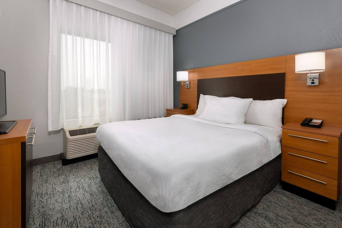 A hotel room with a large bed, a bedside table with a lamp, a heater, and a TV on a stand.