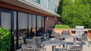 Un patio al aire libre con sillas de mimbre, mesas redondas y una parrilla.
