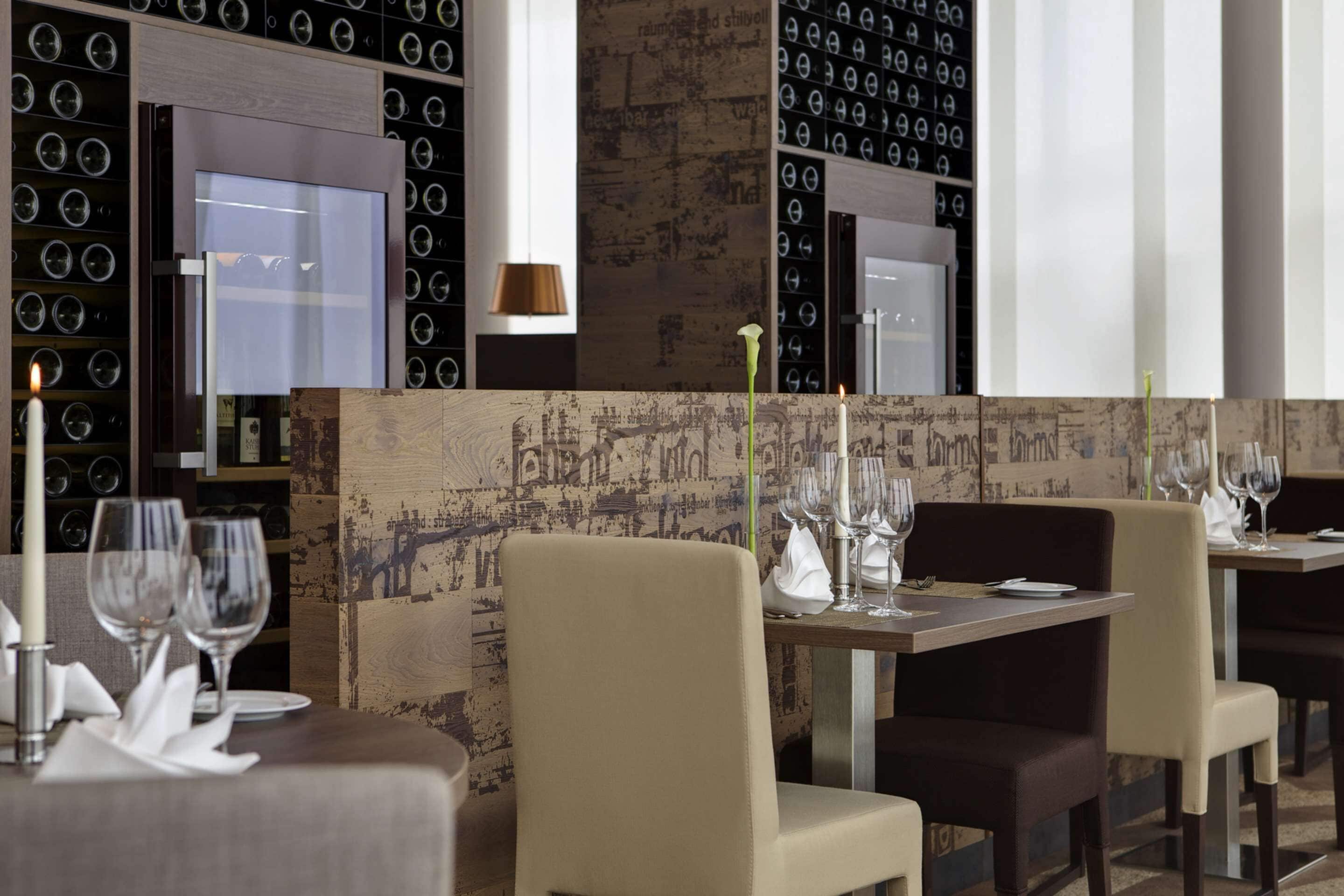 A restaurant with a modern interior, featuring a wall with circular patterns and a textured wall design. Tables are set with wine glasses and plates, and there are chairs around the tables.