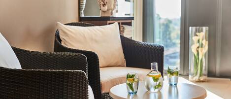 A wicker chair with a cushion, a round table with two glasses of water and a bottle, and a statue in the background.