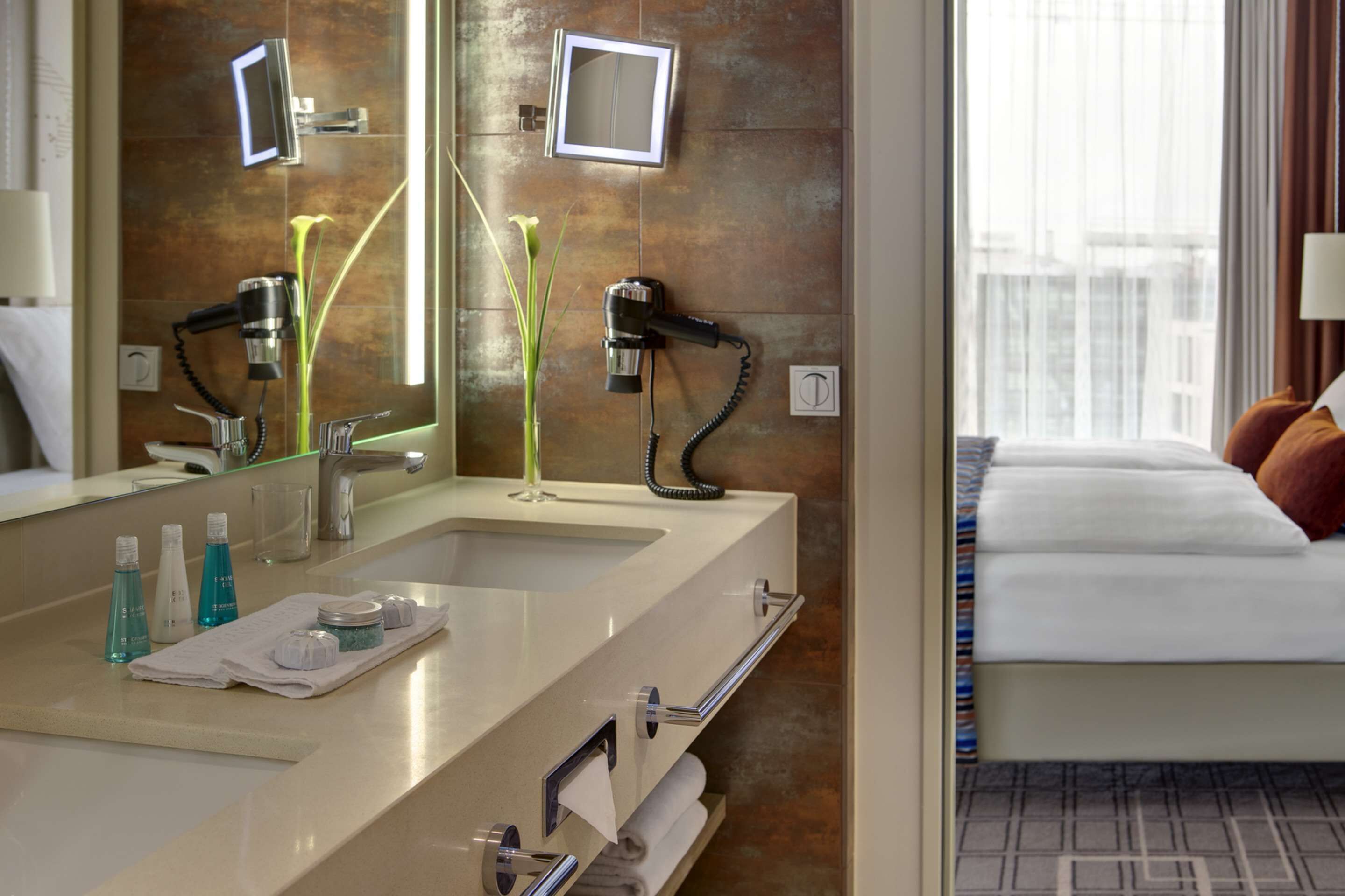 Un baño de hotel con un espejo grande, lavamanos dobles y un tocador con artículos de aseo.