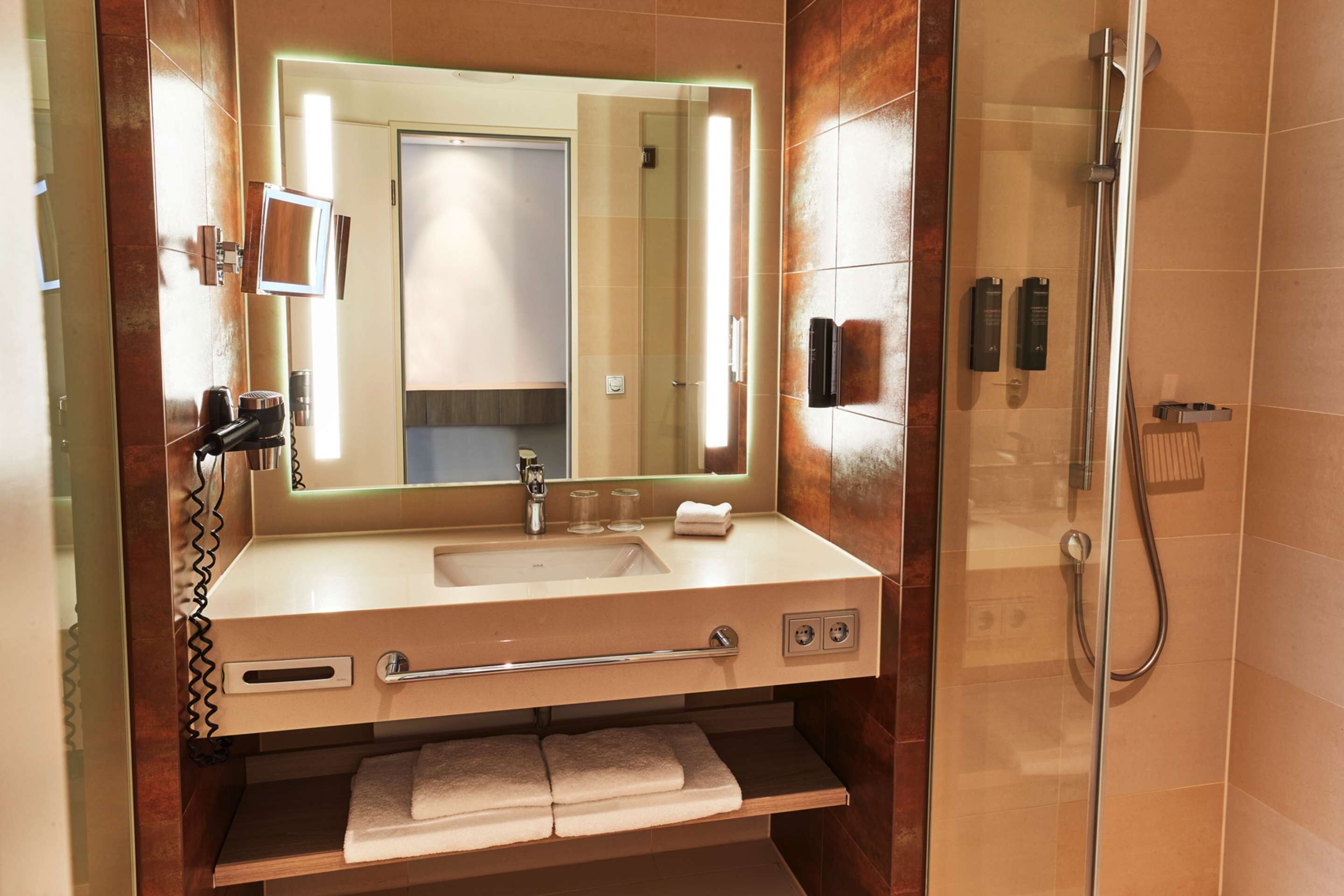 A modern bathroom with a large mirror, sink, and shower.